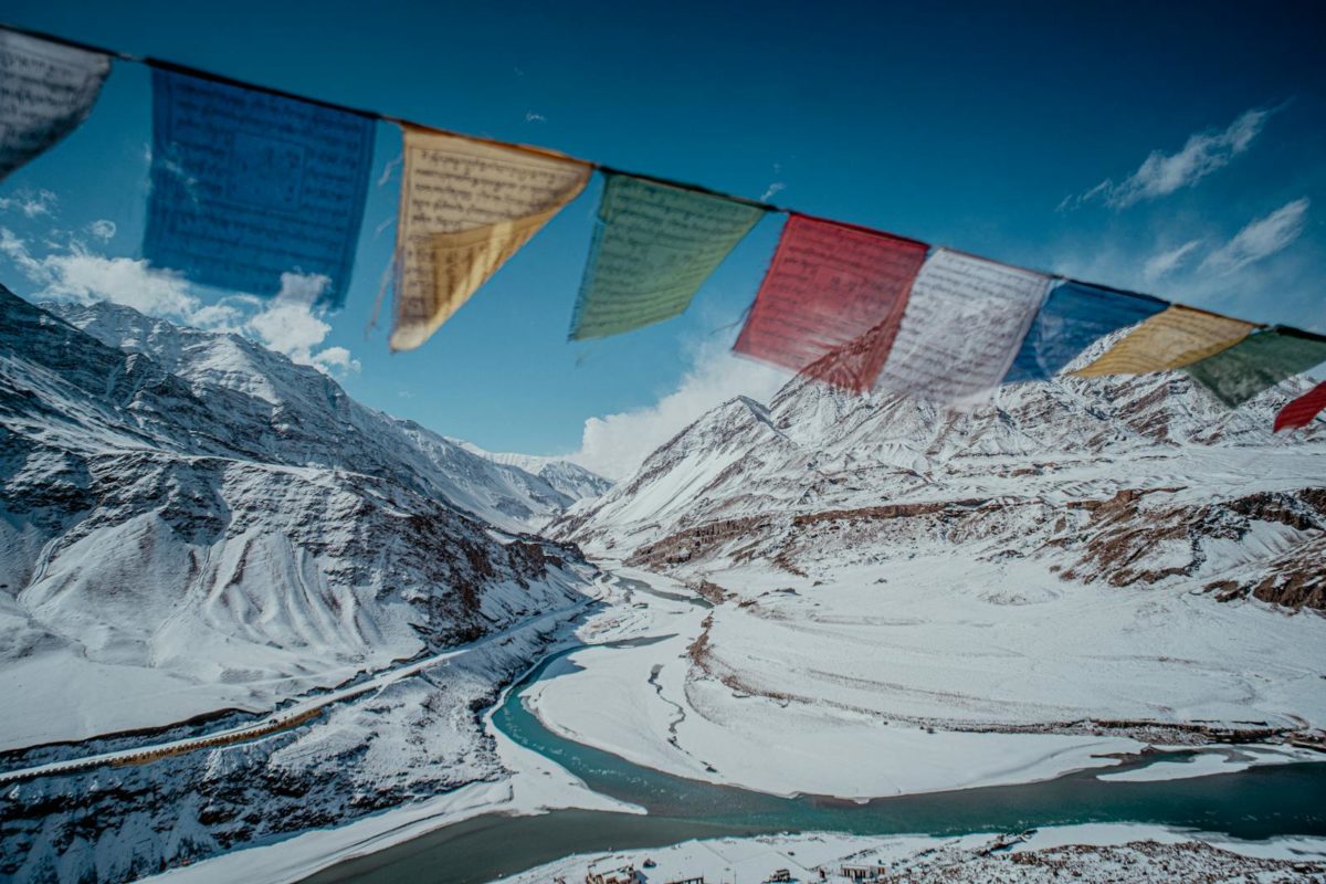 Snow-covered Himalayan mountains with colorful prayer flags under clear blue sky.